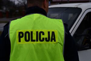 Na zdjeciu stojący tyłem umundurowany policjant, w żótej odblaskowej kamizelce z nasionem policja na plecach.