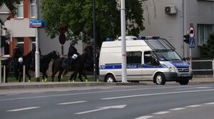Na zdjęciu policyjny radiowóz, za nim policjanci i kibice.