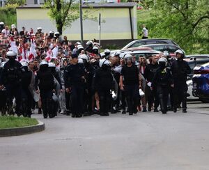 Na zdjęciu umundurowani policjanci, za mini kibice.