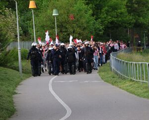 Na zdjęciu umundurowani policjanci, za nimi kibice.