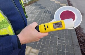 Na zdjęciu policjant trzyma w ręce tarczę do zatrzymywania pojazdów i urządzenie do kontroli stanu trzeźwości.