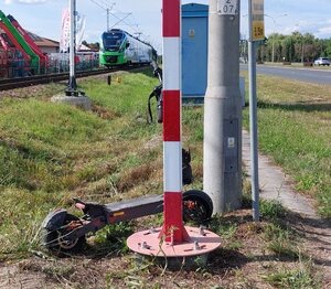 Na zdjeciu tory kolejowe, na których stoi szynobus, przed nim o słup oparta jest hulajnoga elektryczna.